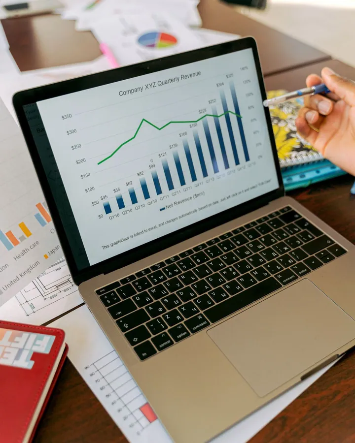 Laptop displaying business charts beside a notebook