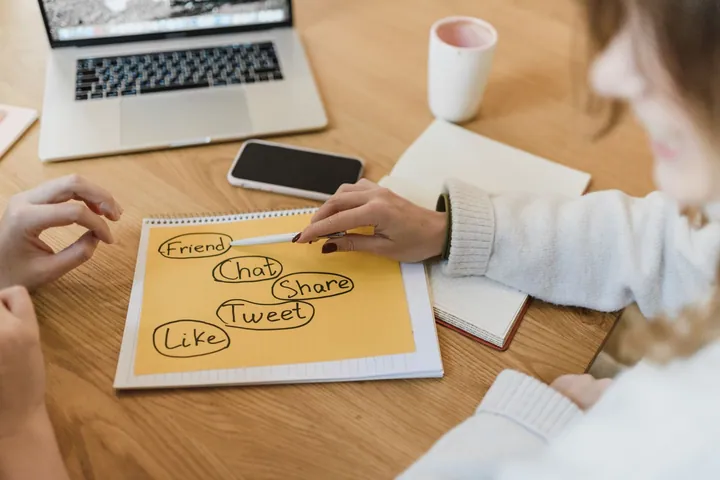 People reviewing social media ideas in a notebook beside a laptop